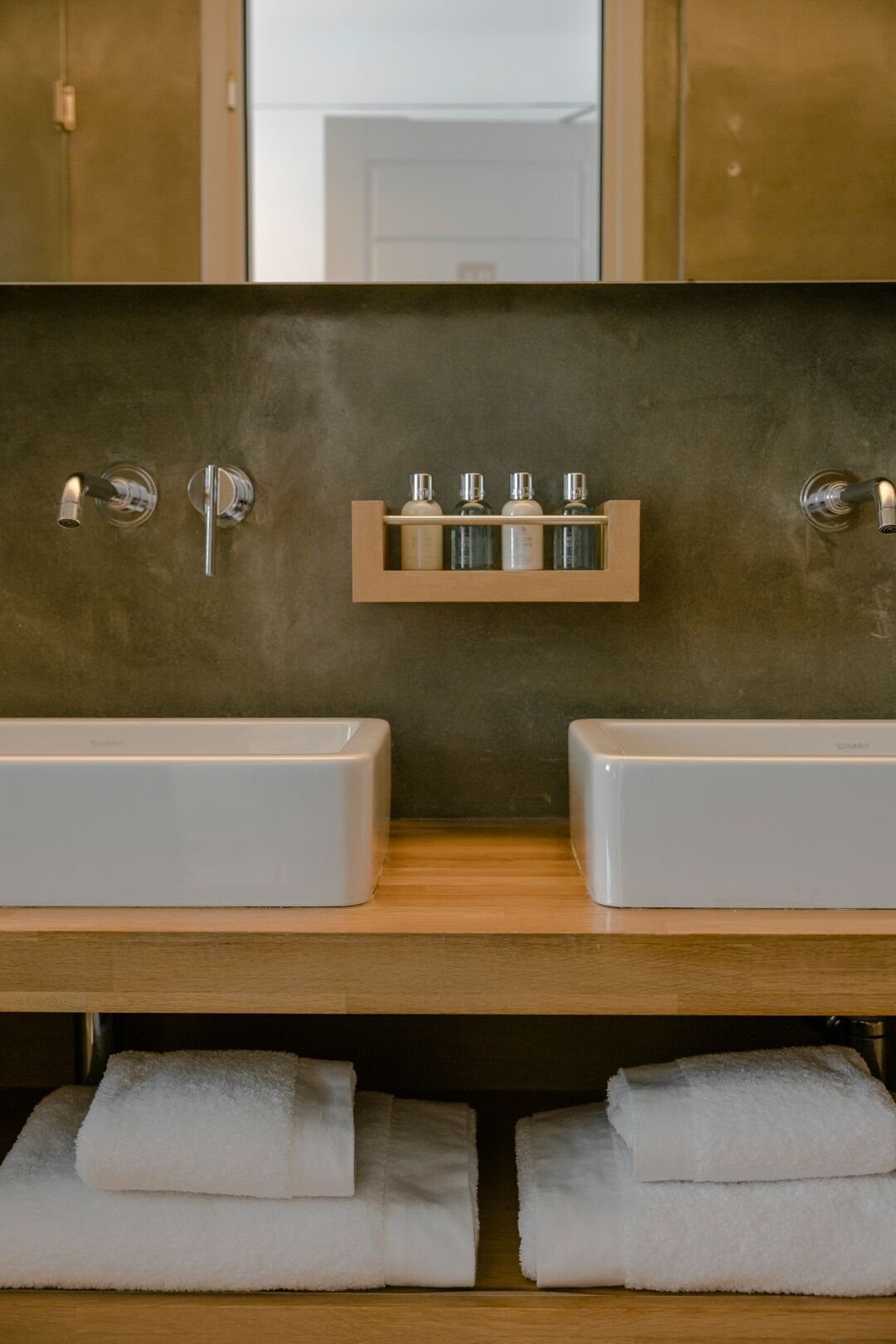 A bathroom with two sinks, a mirror, and a shelf with toiletries.