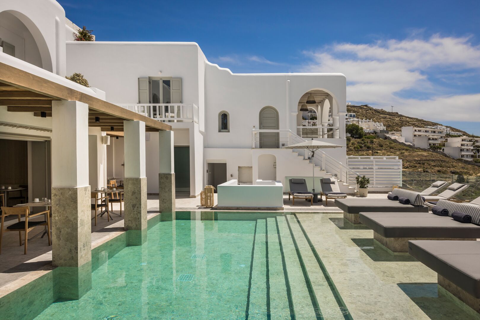 Un espace piscine avec des chaises longues et un coin repas avec des tables et des chaises.