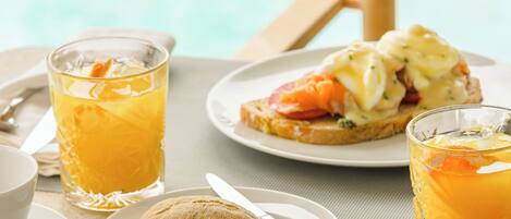 A breakfast setting with a plate of eggs benedict, a croissant, and a glass of orange juice.