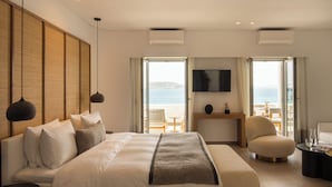 A hotel room with a large bed, a desk, a chair, and a TV. There are large windows with a view of the sea. - Grace Mykonos (Mykonos)