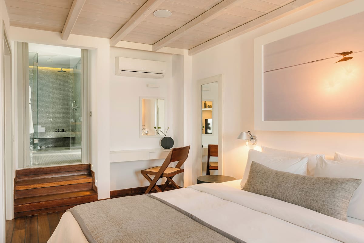 A modern hotel room with a bed, a chair, a desk, and a glass-enclosed shower area.