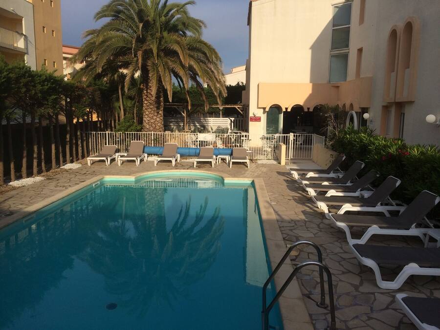Una piscina con sillones de descanso, palmeras y un deck de baldosas de piedra.