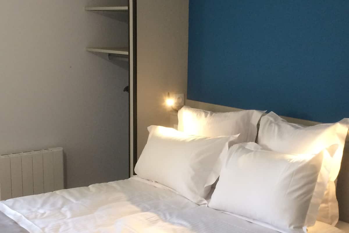 A neatly made bed with white linens and pillows, a white wardrobe, and a blue wall.