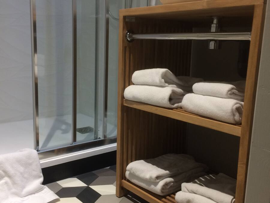 Une salle de bain avec une douche, une étagère en bois avec des serviettes et un carrelage à carreaux.