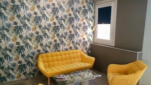 A room with a yellow sofa, a matching armchair, and a glass coffee table. - Hôtel Azur (Agde)
