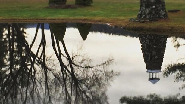 A serene landscape with a pond reflecting trees and a building with a distinctive tower. - Jack O'Lantern Resort and Golf Course (North Woodstock)
