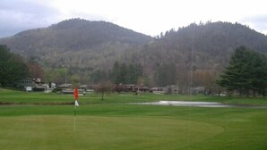 A golf course with a flagstick, a pond, and houses in the background. - Jack O'Lantern Resort and Golf Course (North Woodstock)