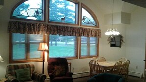 A dining area with a table and chairs, a lamp, and a view of trees through large windows. - Jack O'Lantern Resort and Golf Course (North Woodstock)