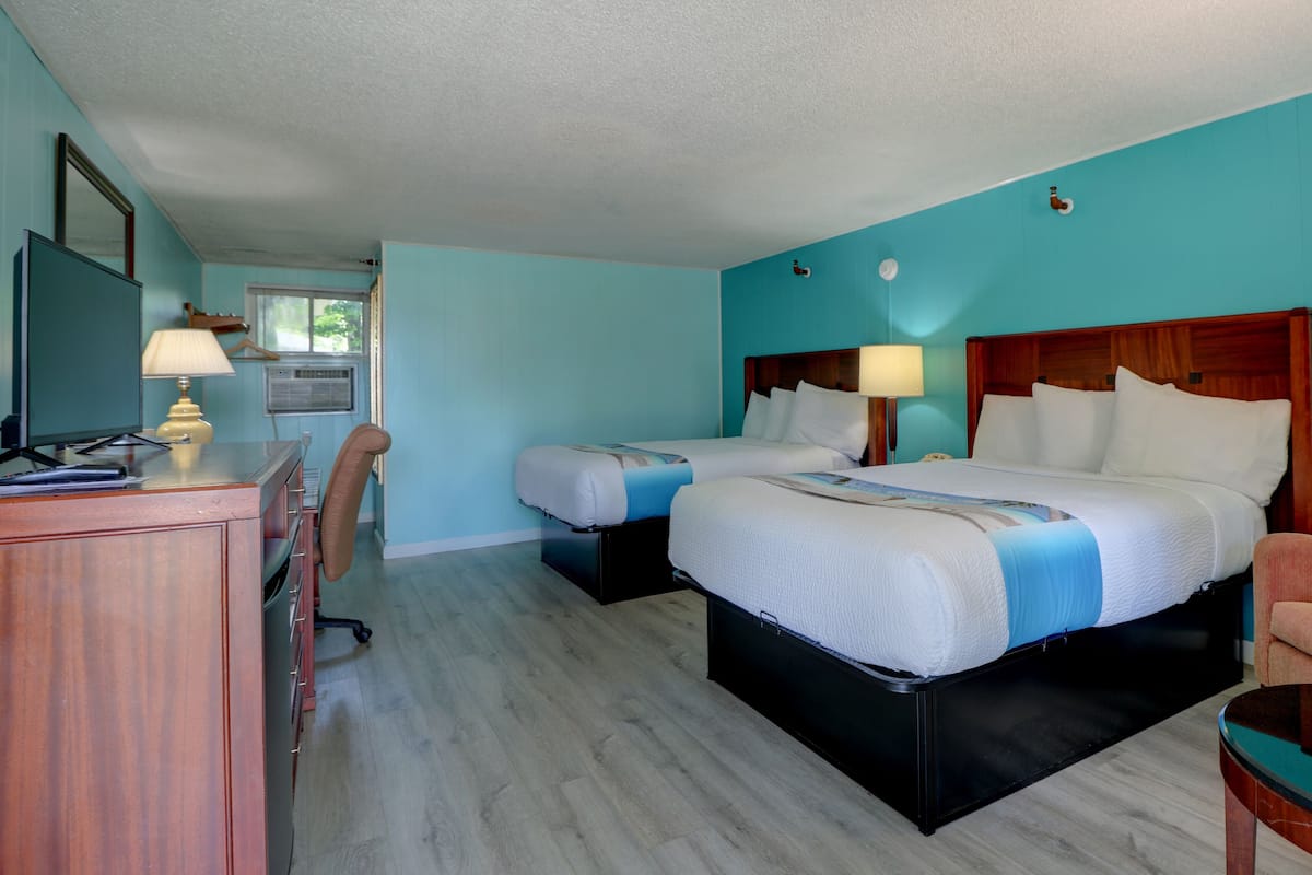 A hotel room with two beds, a desk with a lamp, a chair, and a small table.