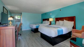 A hotel room with two beds, a desk with a lamp, a chair, and a small table.