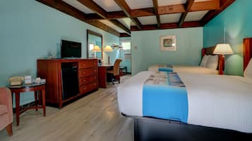 Une chambre d’hôtel avec un plafond en bois, un lit recouvert d’une couverture bleue, un bureau avec une lampe, une chaise et un téléviseur.