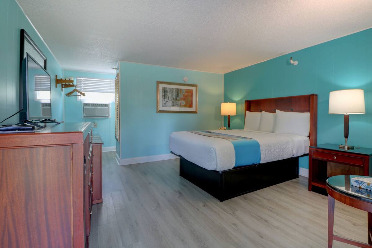 A hotel room with a bed, bedside tables, a desk, a mirror, and a window with blinds.