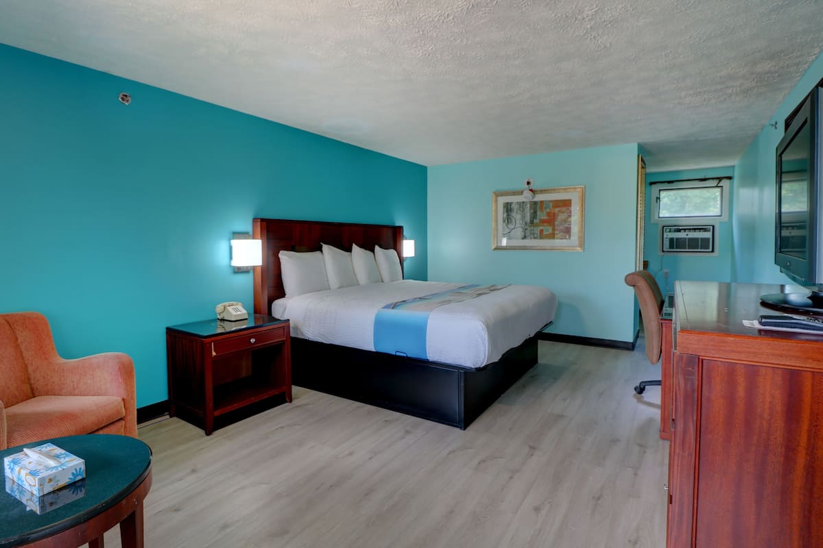 A hotel room with a bed, a nightstand, a desk, a chair, and a television.