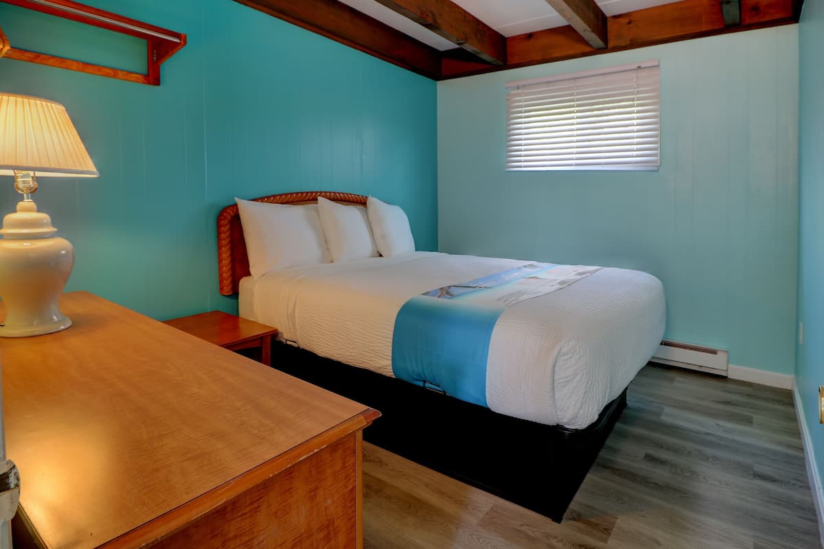 A bedroom with a bed, a nightstand, a lamp, and a window with blinds.