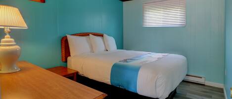 A bedroom with a bed, a nightstand, a lamp, and a window with blinds.