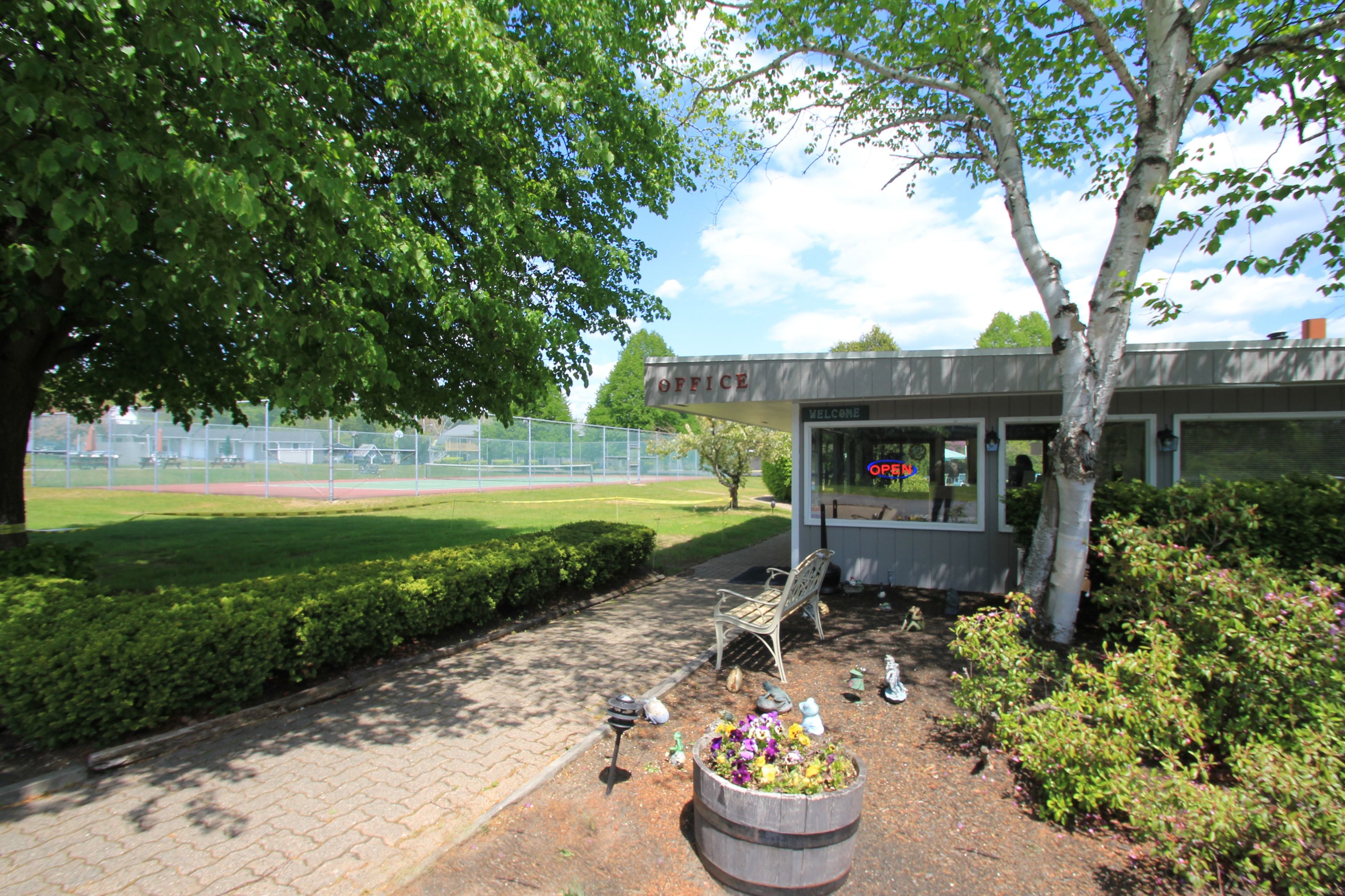 A building labeled "OFFICE" with a "WELCOME" sign, a bench, a bird feeder, and a flower pot.