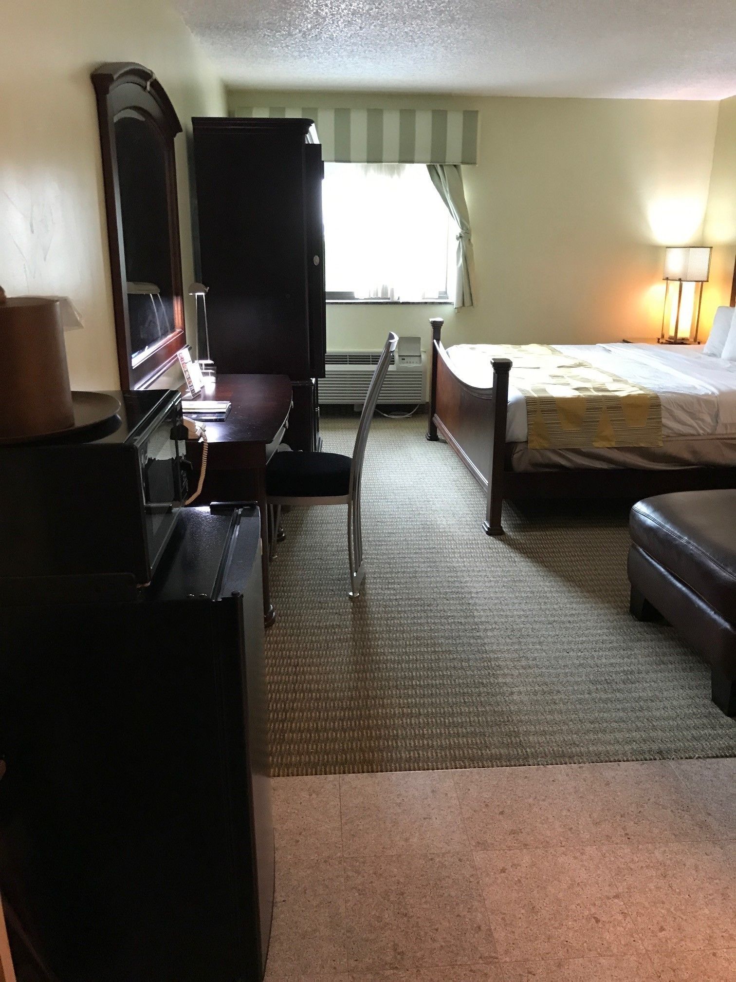 A hotel room with a bed, a desk, a chair, a dresser, and a window with curtains.
