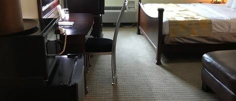 A hotel room with a bed, a desk, a chair, a dresser, and a window with curtains.