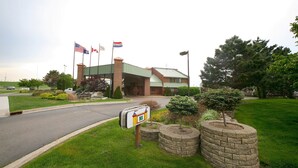 A hotel entrance with a welcoming sign, multiple flags, and a well-maintained lawn.