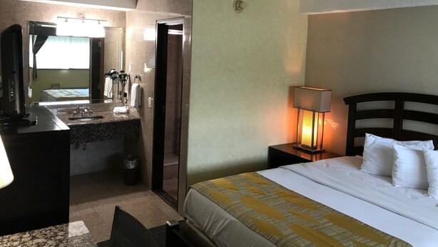 A hotel room with a bed, a desk with a mirror, a sink, and a nightstand with a lamp.