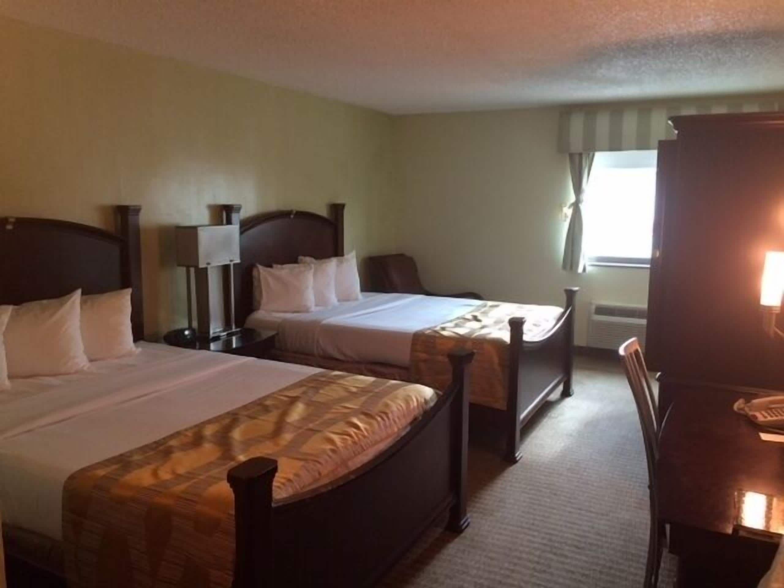 A hotel room with two single beds, a desk, a chair, a lamp, and a window with curtains.