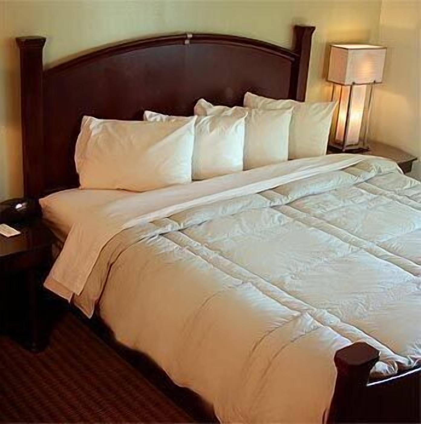 A neatly made bed with a wooden headboard, white bedding, and a bedside lamp.