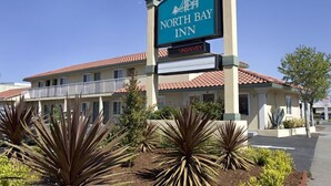 A North Bay Inn sign with a vacancy message, surrounded by landscaping and a building with a red-tiled roof. - North Bay Inn (San Rafael)