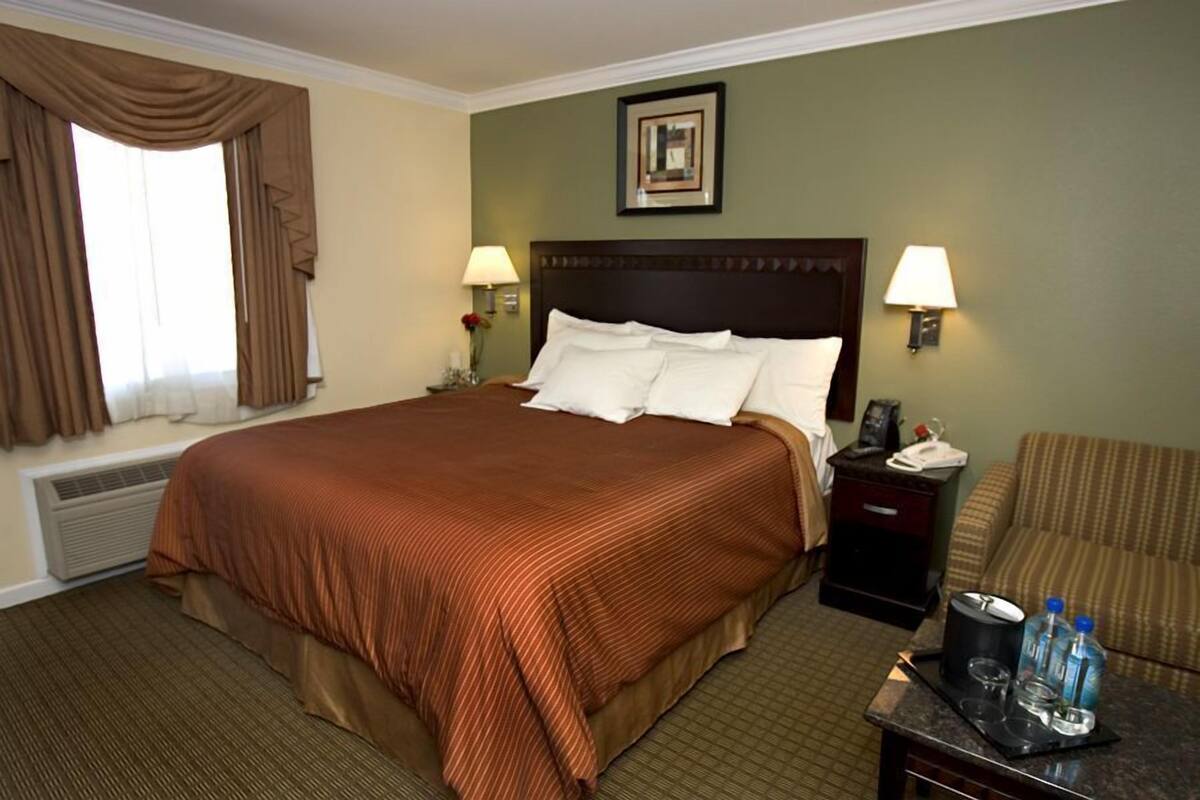 A hotel room with a large bed, two bedside tables with lamps, a chair, and a small table with a tray.