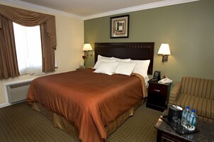 Quarto de hotel com uma cama grande, duas mesas de cabeceira com abajures, uma cadeira e uma mesinha com bandeja.