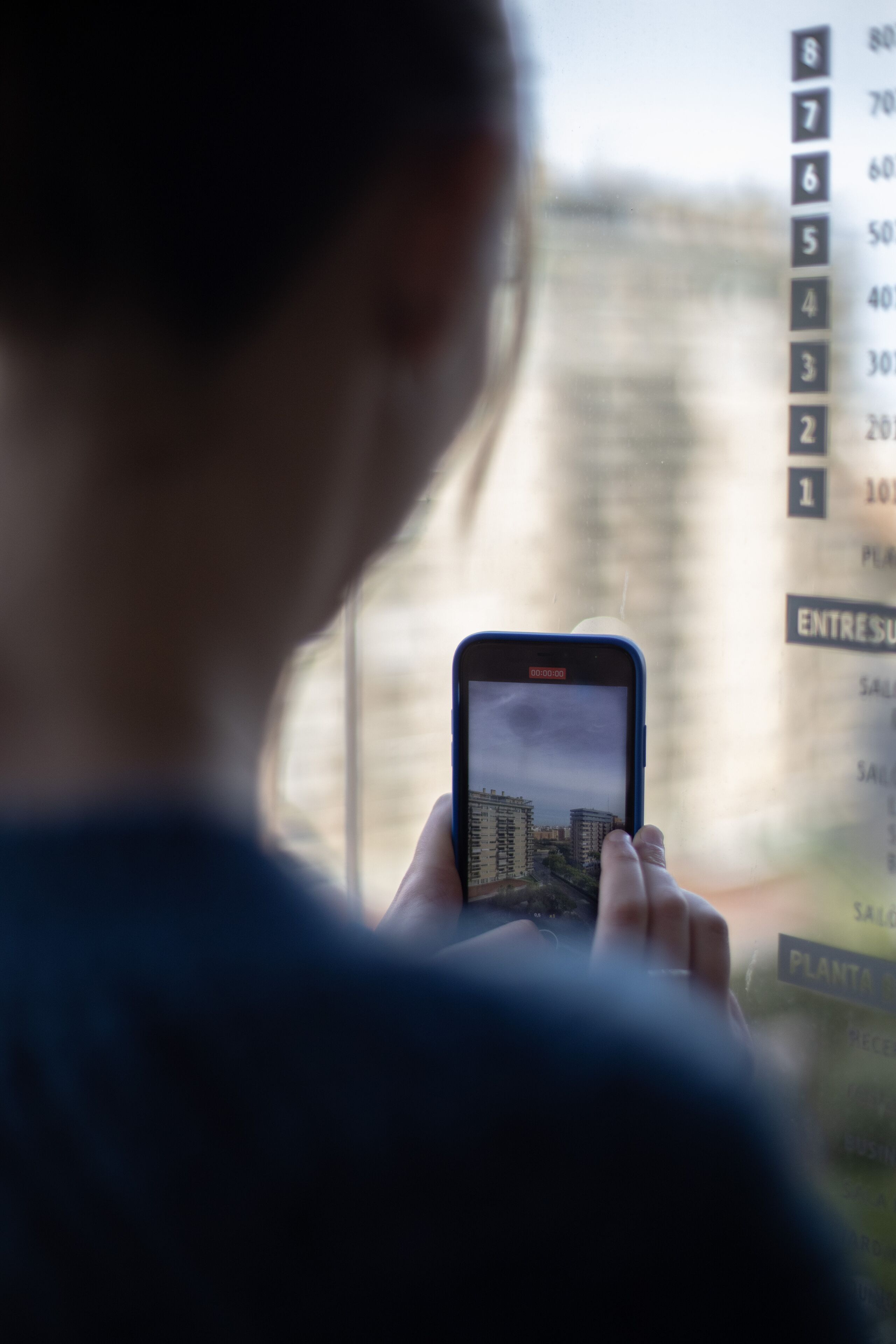 Una persona sosteniendo un teléfono inteligente con una vista urbana en la pantalla, visible a través de una ventana con fondo desenfocado.