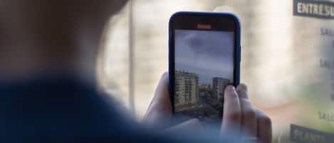 Una persona sosteniendo un teléfono inteligente con una vista urbana en la pantalla, visible a través de una ventana con fondo desenfocado.