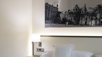 A hotel room with a bed, a nightstand, a lamp, and a wall-mounted picture of a cityscape.