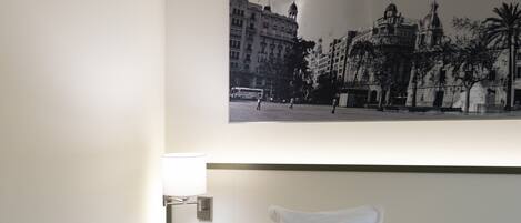 A hotel room with a bed, a nightstand, a lamp, and a wall-mounted picture of a cityscape.