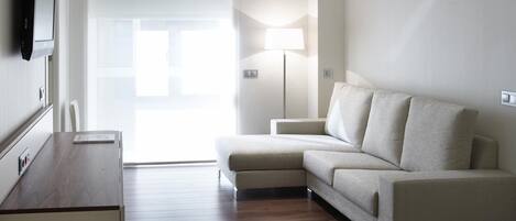 A modern living room with a sofa, a flat-screen TV mounted on the wall, and a wooden floor.