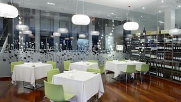 Un interior de restaurante con varias mesas y sillas, una estantería para vinos y decoración en las paredes.