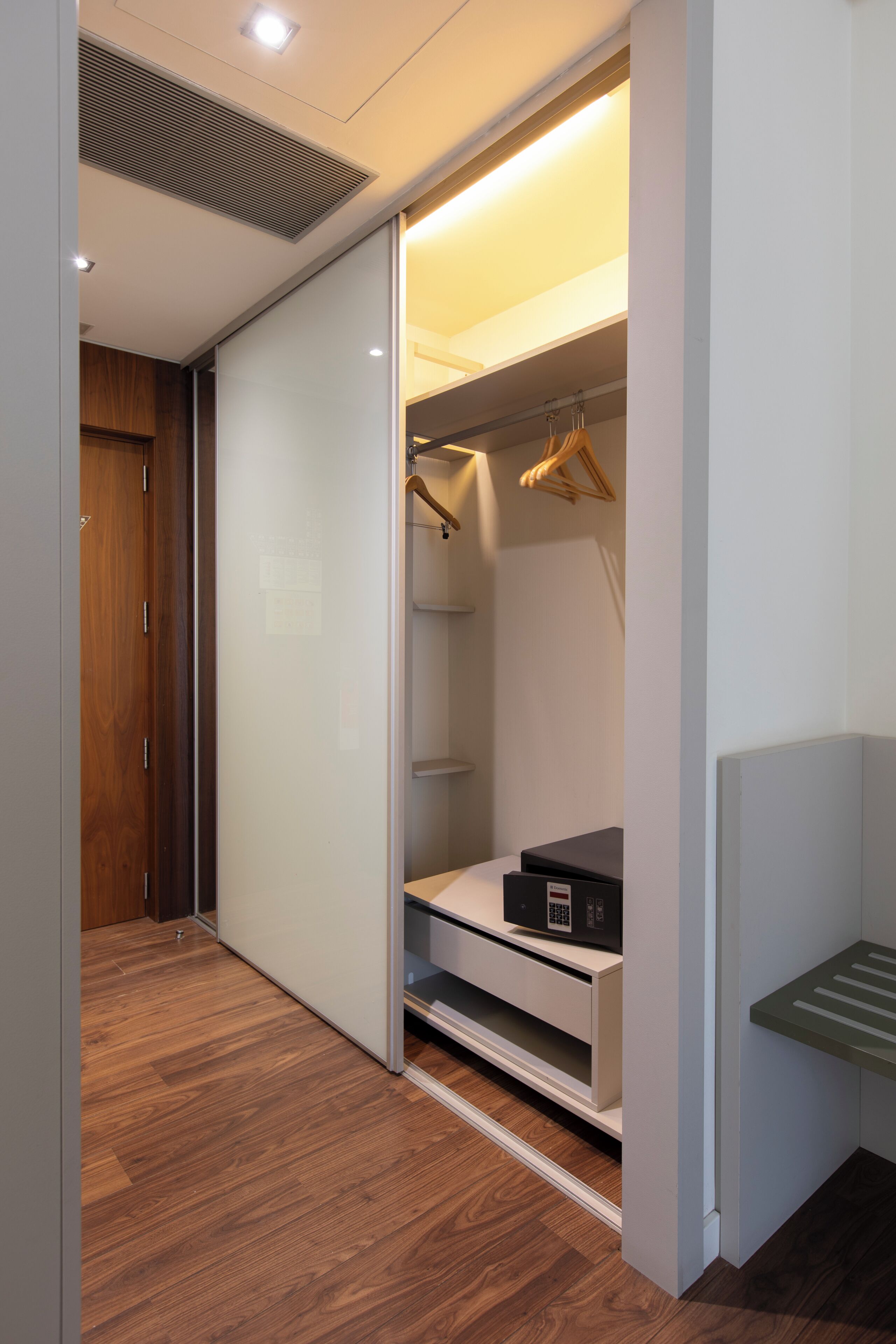 Vestidor con puerta corredera, piso de madera e integrado un banco con espacio de almacenamiento.