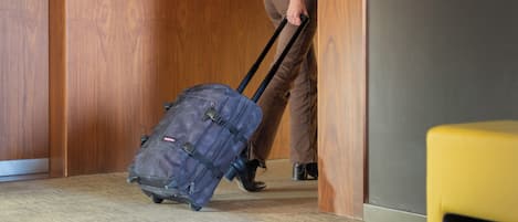A person pulling a suitcase through a hallway with wooden walls and a sign indicating an emergency exit.
