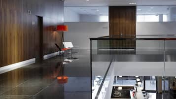 En moderne hotellobby med glasgelænder, et siddeområde med rød lampe og udsigt til et lavere plan.