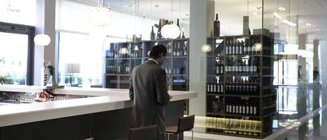 A modern bar area with a man standing at the counter, bar stools, and shelves of bottles.