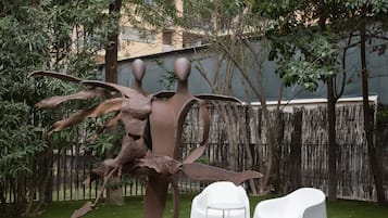 A sculpture of a human figure with outstretched arms, surrounded by a grassy area with two white chairs.