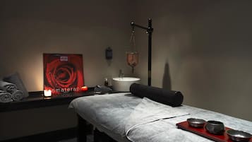 Un cuarto de spa con una camilla de masaje, toallas, una vela, un cartel con motivos de rosas y un elemento decorativo de agua.