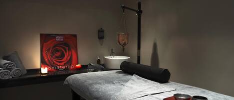 A spa room with a massage table, towels, a candle, a rose-themed poster, and a water feature.