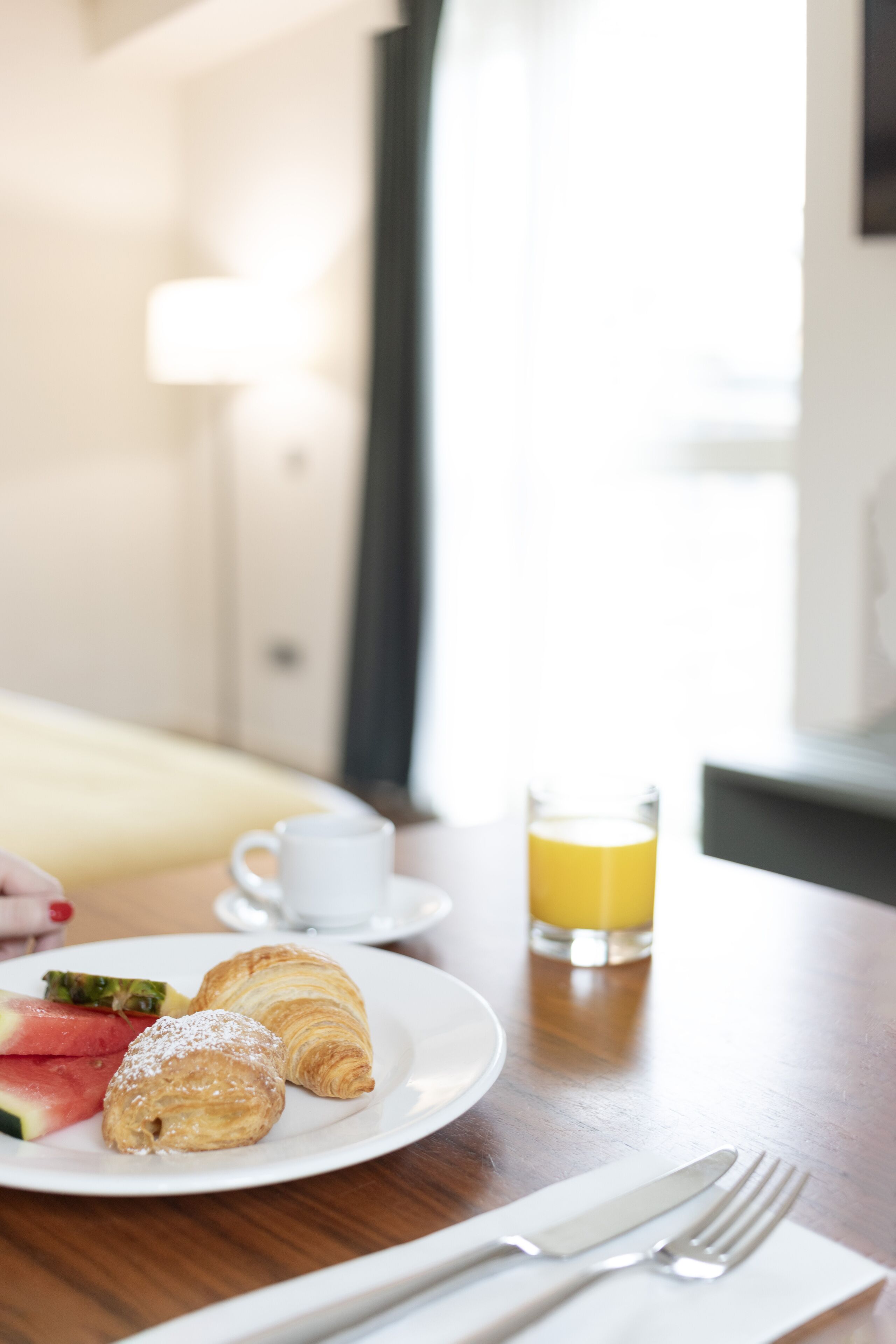Un desayuno con croissants, una fuente de fruta, una taza de café y un vaso de zumo de naranja sobre una mesa de madera.