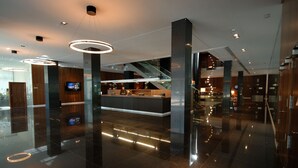 Un vestíbulo de hotel moderno con una recepción, pilares grandes y una escalera.