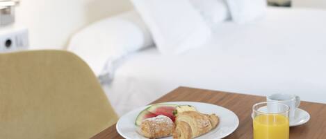 A hotel room with a neatly made bed, a breakfast table with croissants, a glass of orange juice, and a painting on the wall.