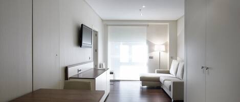 A modern, minimalist living room with a wooden dining table, a sofa, and a TV mounted on the wall.