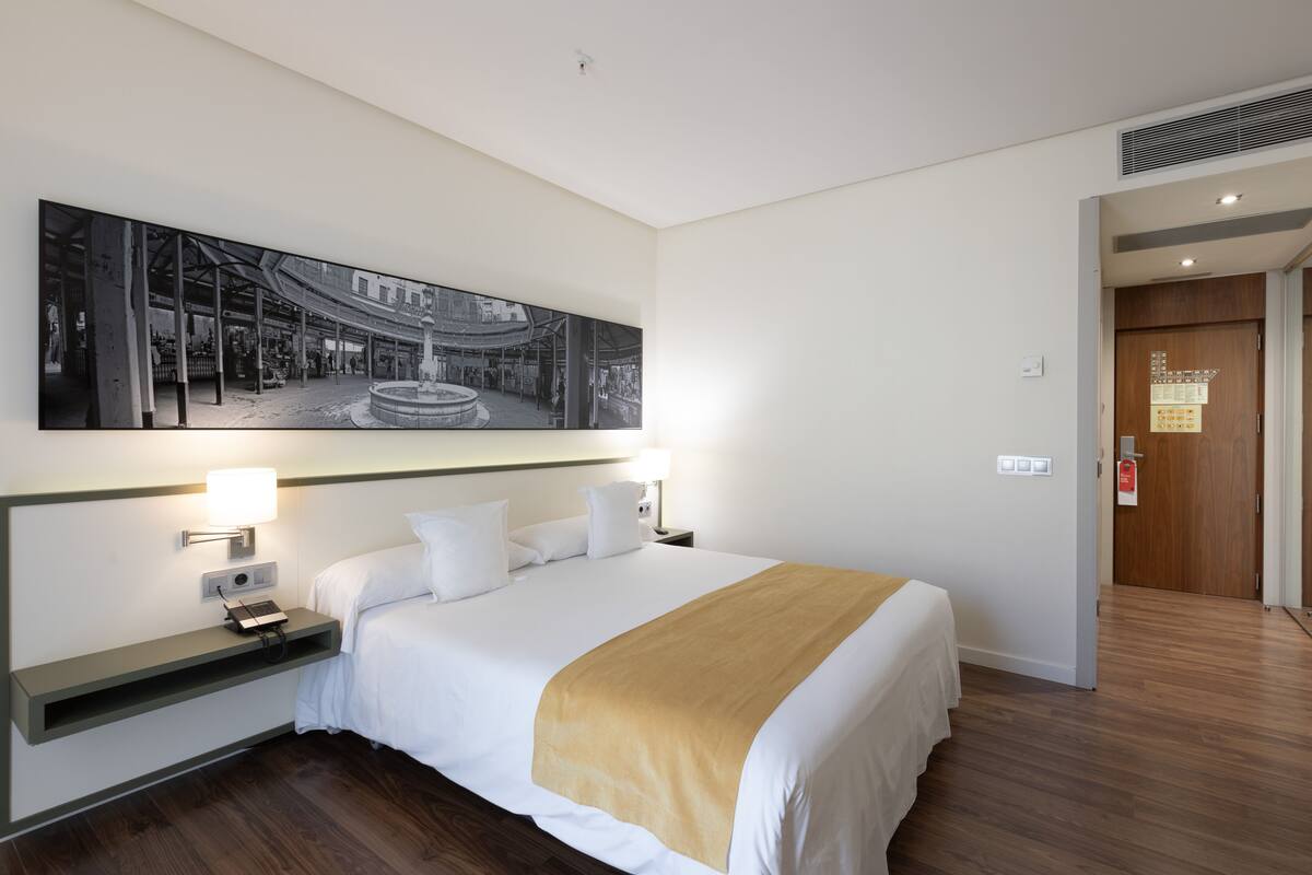 Una habitación de hotel con una cama grande, mesitas de noche con lámparas, una obra de arte colgada en la pared y una puerta de madera.