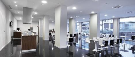 A spacious, modern conference room with a polished black floor, white tables, and chairs, large windows offering a view of the city, and a central wooden reception desk.