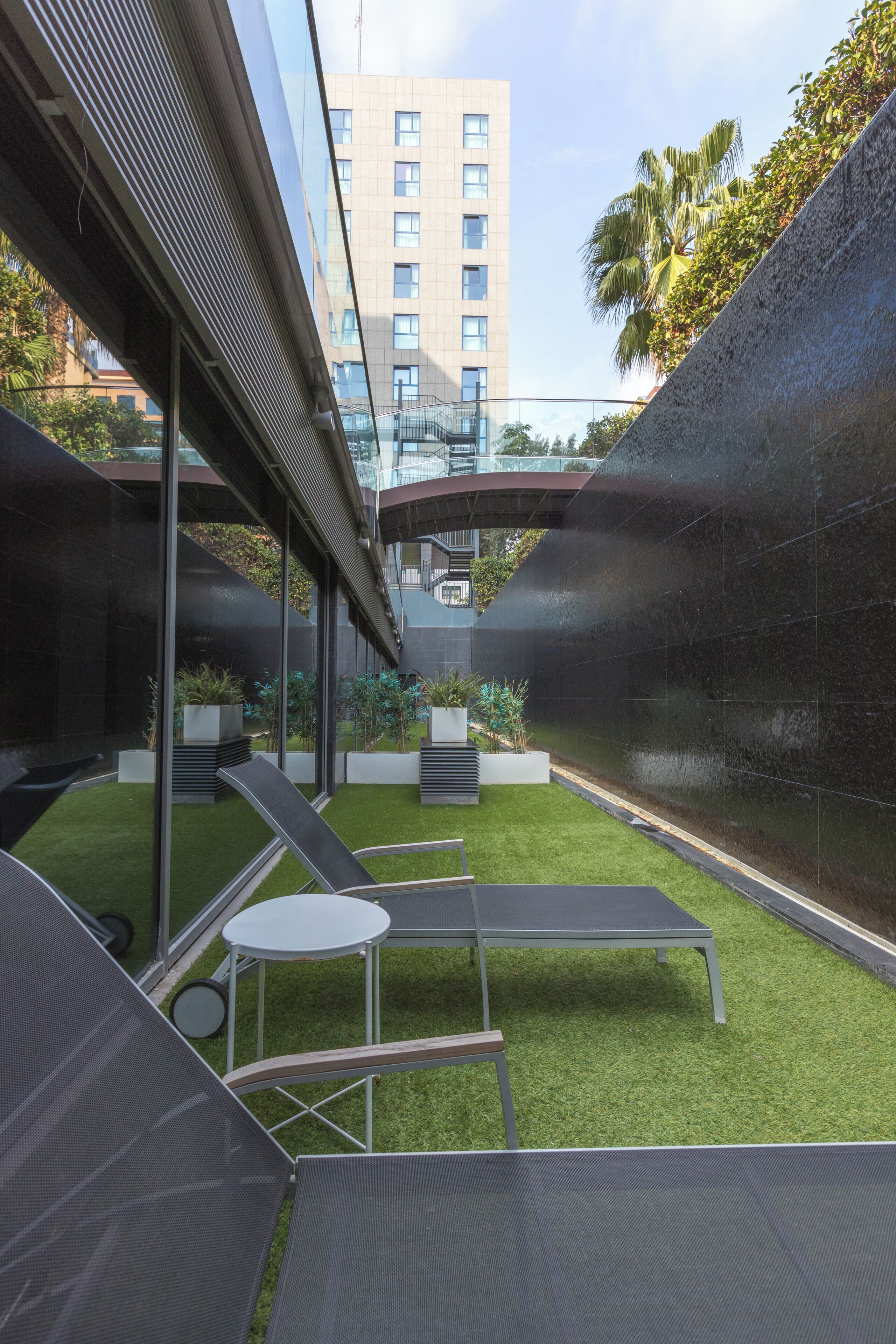 An outdoor lounge area with a glass wall, a pool, and a view of a high-rise building.