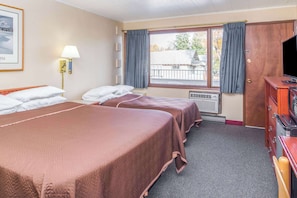 Two single beds with matching bedspreads, a large window with a balcony view, and a wall-mounted lamp.